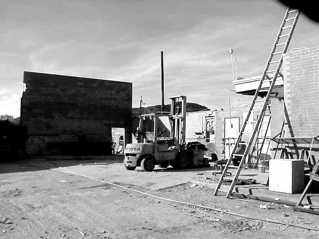 A black and white photo about Sun Valley Construction features a forklift, a ladder propped against a building, and various construction materials scattered around.