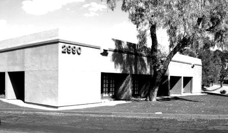 Black and white photograph of a single-story building with the number 2900 on its facade, about Sun Valley Construction, featuring a minimalist architectural style with trees casting shadows on its exterior.