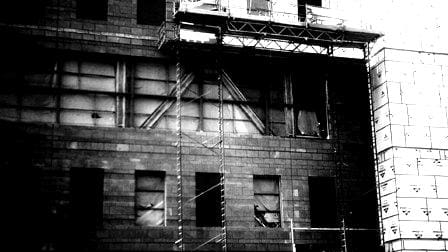 A black and white photograph of a dilapidated building facade with boarded-up windows, visible scaffolding, and signs of neglect about Sun Valley Construction.