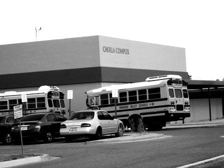 Black and white photo of two parked buses in front of a building with a sign that says "Cholla Complex about Sun Valley Construction".