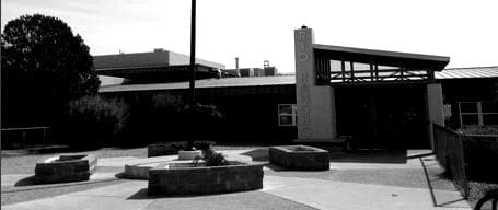 A black and white photograph of a courtyard with square benches and a planter, about Sun Valley Construction, featuring a building with a prominent, symmetrical entrance in the background.