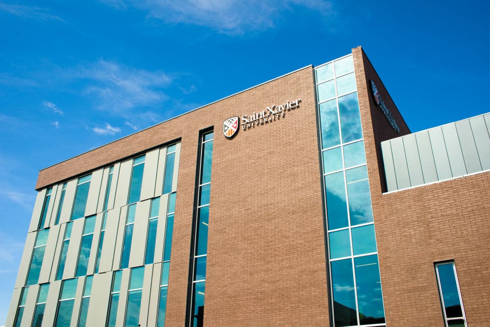 Modern university building with a brick facade and large windows under a blue sky with scattered clouds. the name "saint xavier university" is prominently displayed on the exterior wall.