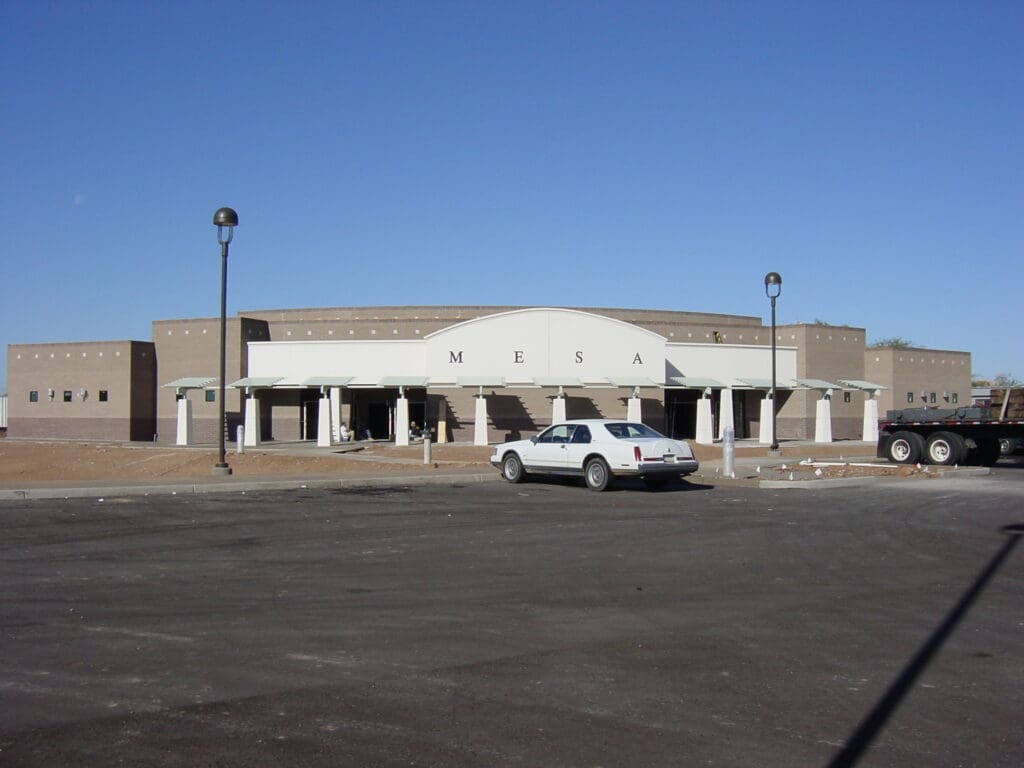 A newly constructed building with a sign reading "mesa" above the entrance, featuring a large parking lot with a single car parked near the front.