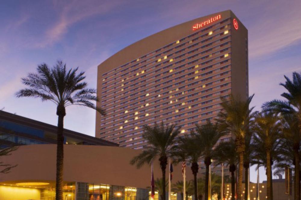 A sheraton hotel building at dusk with illuminated windows, flanked by palm trees.