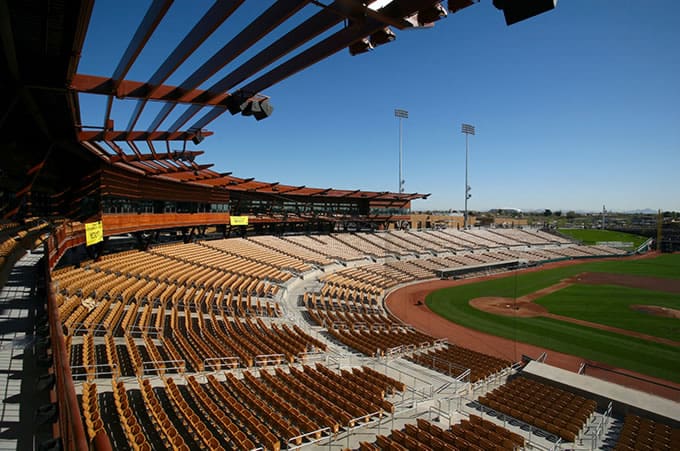A sunny day at an empty baseball stadium with rows of brown and tan seats overlooking the field.