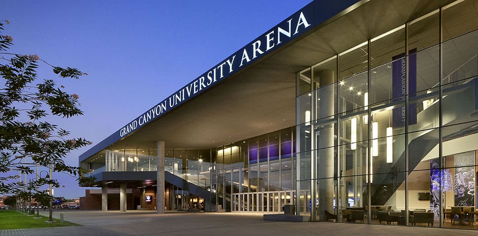 Modern arena facility at dusk with illuminated interior lights and prominent signage for grand canyon university arena.