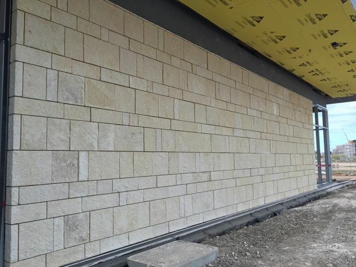 A section of a building under construction showing an insulated wall with stone veneer cladding and exposed structural elements on the right side.