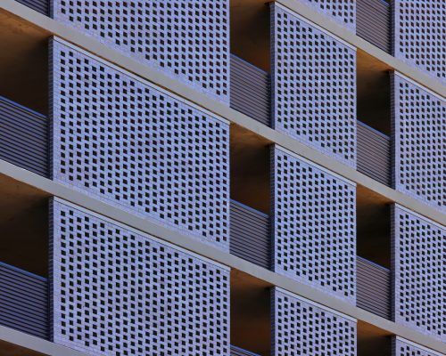 Close-up of a modern building facade featuring repetitive geometric patterns of blue balconies with perforated metal railings.