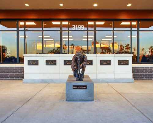 Bronze statue of a firefighter in full gear, kneeling in front of a building, with memorial plaques displayed on pedestals.