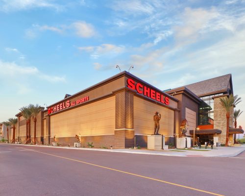 Exterior view of a large scheels sporting goods store with a clear blue sky at dusk.