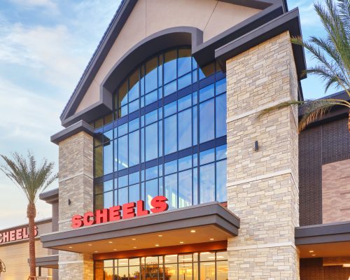 Exterior view of a scheels store featuring modern architecture with large glass windows and stone walls, set against a clear sky at dusk.