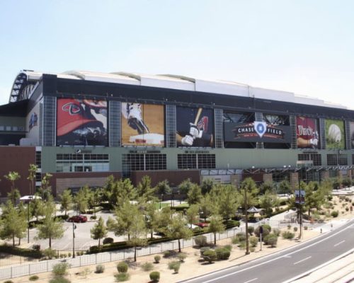 Exterior view of chase field, a baseball stadium with large banners featuring arizona diamondbacks branding, set against a clear sky.
