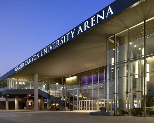 Modern arena facility at dusk with illuminated interior lights and prominent signage for grand canyon university arena.