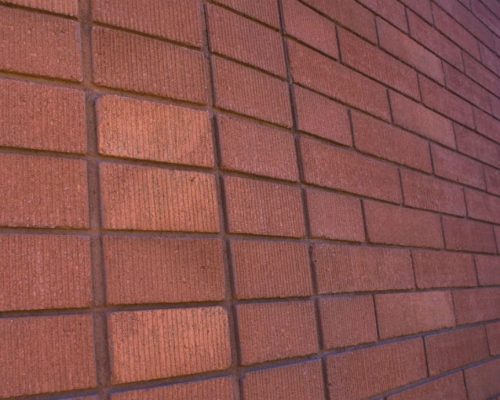 Texture of a red brick wall with the focus on the bricks' pattern and surface details, photographed at an angle.