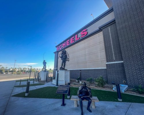Exterior view of a scheels store with statues and a bench in front.