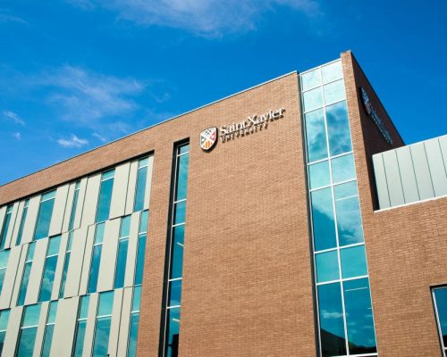 Modern university building with a brick facade and large windows under a blue sky with scattered clouds. the name "saint xavier university" is prominently displayed on the exterior wall.