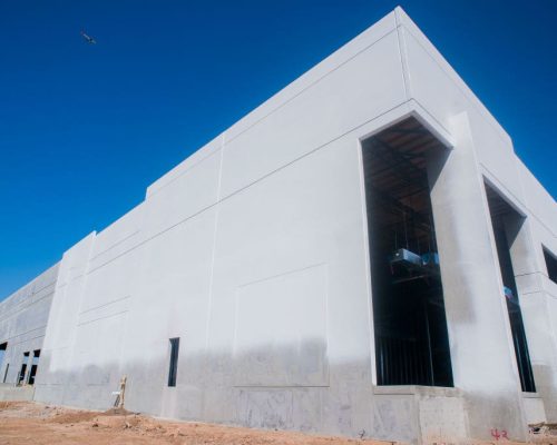 A partially constructed industrial building with large open doorways under a clear blue sky.